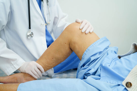 Doctor checking Asian elderly woman patient with scar knee replacement surgery in hospital.