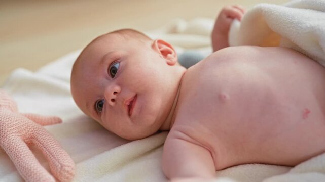 Baby girl sucking finger on soft blanket in studio beside pink plush toy, lying and looking up; gentle bonding serenity.