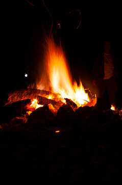 Large burning bonfire at night with distant person