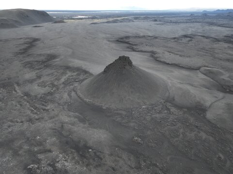 Aerial view of a volcanic cone rising from the barren, dark volcanic landscape with rugged terrain and vast horizons in Fljotsdalsherad, Mulathing, Iceland.