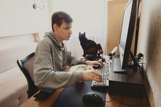 Young person working on computer at home desk with cat companion