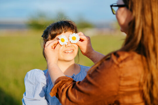 Mother holding daisy flowers over daughter's eyes outdoors