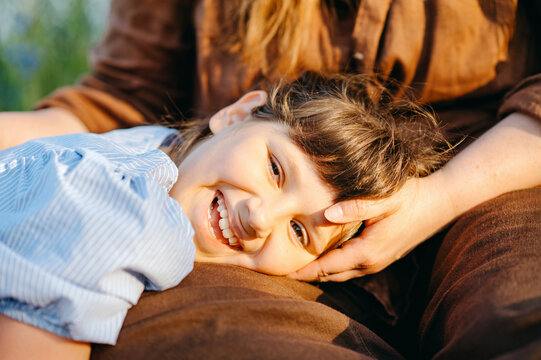 Smiling young girl resting on mother's lap outdoors