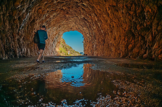 Man walks through a wet rock tunnel towards daylight, Zingaro
