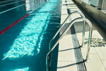 Indoor swimming pool ladder standing beside lane water in training facility, supporting children learning to swim. Useful for swim school, water safety, youth sports promotion © pressmaster