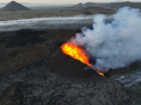 Aerial view of the Litli-Hrutur volcanic eruption with glowing lava flowing from the crater and thick smoke plumes rising over the rugged volcanic landscape, Grindavik, Grindavikurbaer, Iceland.