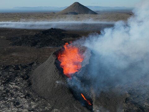Aerial view of Litli-Hrutur volcanic eruption with glowing lava flowing from the crater and thick smoke rising over the rugged landscape in Grindavik, Grindavikurbaer, Iceland.