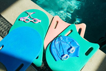 Naklejka premium Close up of childrens swimming lesson gear resting by pool, showing kickboards, goggles, swim cap for training and water safety. Useful for swim school, youth sports, fitness promotion
