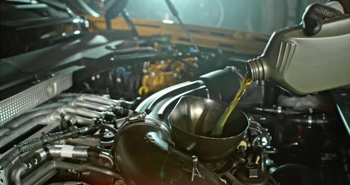Super slow motion wide shot of mechanic pouring motor oil into car engine, hand visible, camera moving across engine. Automotive maintenance concept, service and repair.