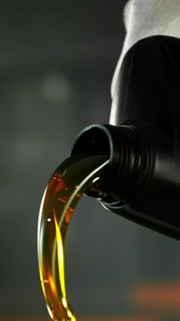 Super slow motion (1000 fps) cinematic shot of motor oil pouring from a container with dynamic camera movement around the bottle neck. Golden liquid flow with bubbles and reflections