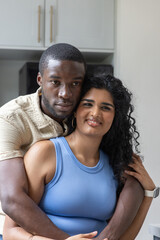 Obraz premium Diverse couple hugging in kitchen man holding Indian woman wearing blue tank, smartwatch visible