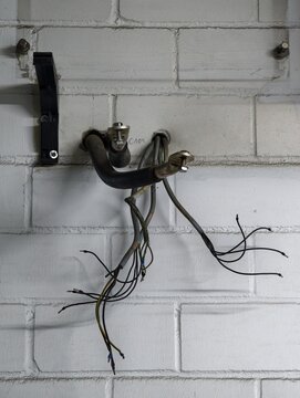 Exposed electrical cables and hydraulic hoses emerging from white painted cinderblock wall