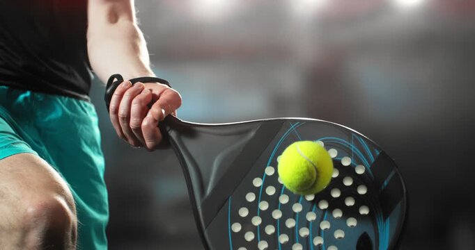Super slow motion close-up of a hand holding a padel racket as a yellow ball hits the surface, filmed at 1000 fps. Dramatic studio lighting highlights the impact, motion of the racket and ball.