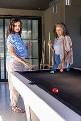 Naklejka premium Diverse female friends standing at black felt pool table, holding cues and examining ball cluster