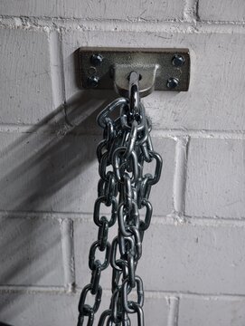 Metal chain hanging from wall bracket against painted brick background with strong directional shadow and industrial texture