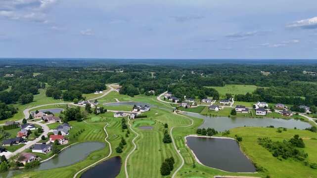 A smooth panoramic drone flight rotating in a slow arc over a country development. The video captures premium villas, scenic water hazards, and manicured lawns under patchy clouds.