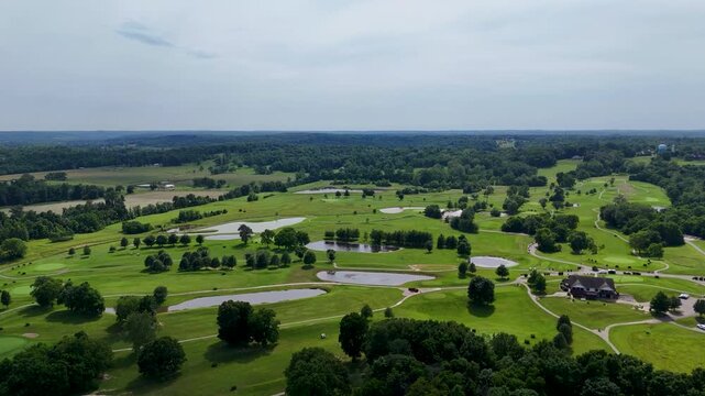 A steady drone flight moving straight over an upscale residential golf community. The video reveals modern luxury houses, winding asphalt paths, and a large communal lake under patchy clouds.