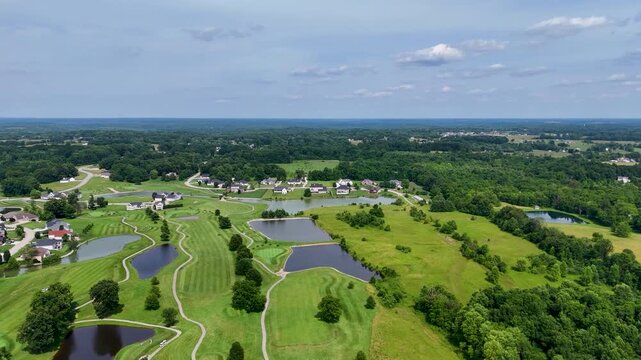 Cinematic high-angle drone flight advancing straight over an expansive country turf. The video captures multiple water reservoirs, winding paths, and a vast green meadow under a bright sky.