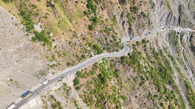 Drone shot of long vehicle queue on narrow cliffside highway pass India.