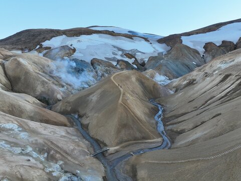 Aerial view of the geothermal landscape of Kerlingarfjoll with steaming vents, snow-capped mountain ridges, and a winding hiking trail in Hveragerdi, Hveragerdisbaer, Iceland.