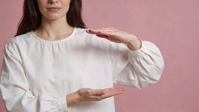 Woman showing size comparison gesture with hands, measuring dimensions concept, scale estimation visual representation, isolated on pink background, minimalist style.