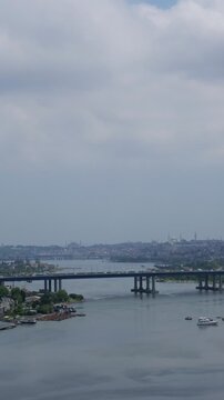 Aerial view of boats sailing on the golden horn waterway with the historic istanbul skyline, including mosques and the ataturk bridge, under a cloudy sky during the day
