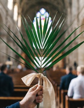 A hand holding a palm frond tied with a ribbon inside a church during palm sunday service