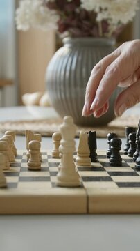 Vertical side view shot of senior people moving chess pieces on wooden board during game. Footage promoting cognitive health programs and active aging lifestyles for elderly people
