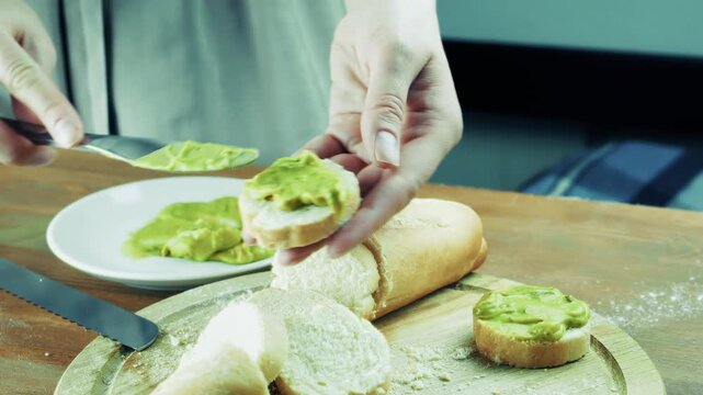 Spreading Green Avocado Guacamole Sauce On Slice Of Fresh Baguette Bread. Healthy Breakfast Snacking 