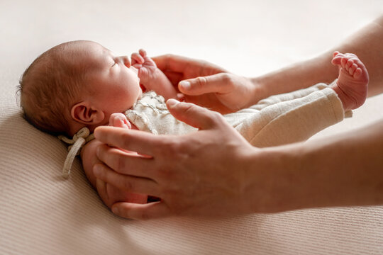 Parent hands gently cradle peaceful newborn baby on soft beige surface.