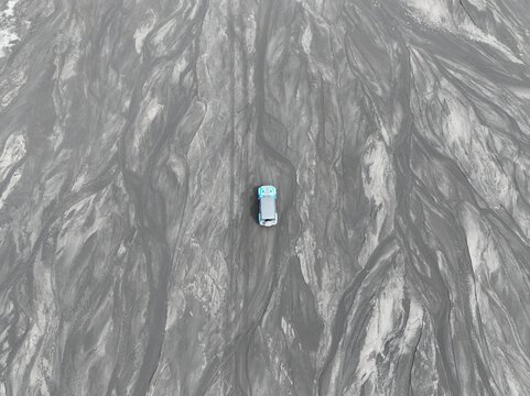 Aerial view of a vehicle driving across the dark volcanic sand patterns of a riverbed in Vik, Myrdalshreppur, Iceland.
