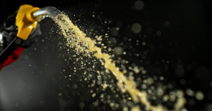 Super slow motion (1000 fps) fuel spraying from gasoline nozzle, dynamic liquid stream and droplets on black background. Dramatic lighting, energy concept, automotive fuel motion.