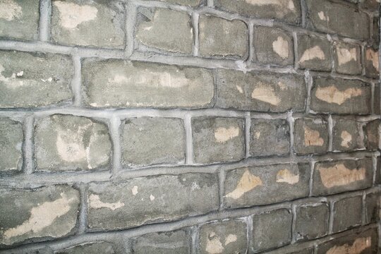 An angled close-up view of an indoor old gray brick wall texture with concrete seams and rows of blocks for building interior background pattern structure framework material layout context detail