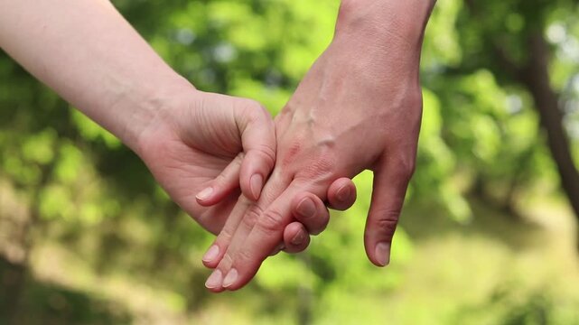 Close-up of two women's hands holding each other. Two women holding hands against a background of nature. A symbol of trust, tenderness and LGBT relationships. Concept of love and equality