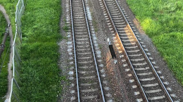 Railway tracks from above, surrounded by green grass, with transport infrastructure and train route in the background