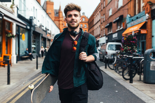 Ireland, Dublin, portrait of young man with skateboard walking on the street