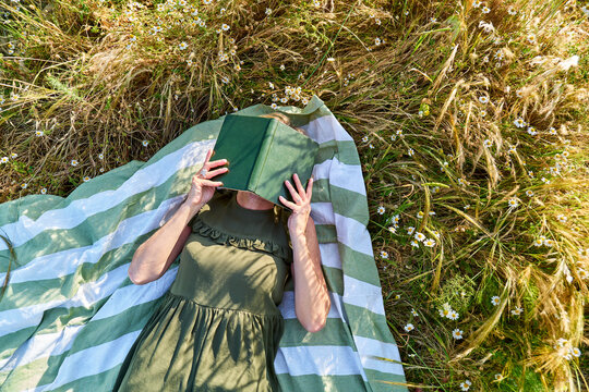 Woman relaxing under a book on a blanket in a summer meadow