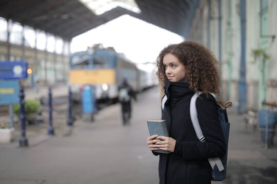 Thoughtful woman holding a book on a train platform