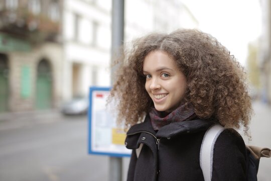 Young woman with curly hair smiling on a city street