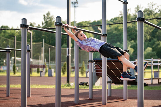 Young boy hangs from pull up bar at outdoor gym