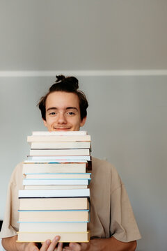 Happy teenager holding a large stack of books