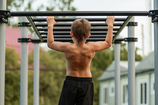 Young boy shows back muscles on monkey bars