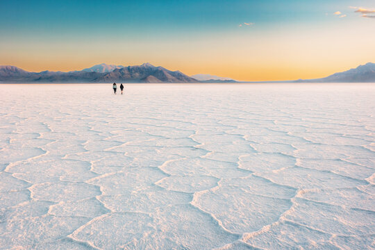 Two people walking across the Bonneville Salt Flats at sunset