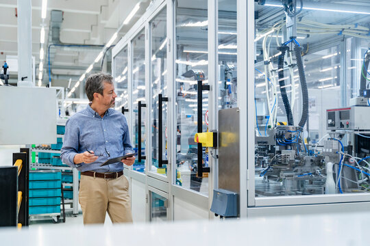 Engineer with tablet inspecting automation machinery in factory