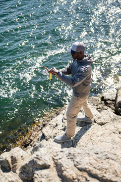 Black man fishing from a rocky coast