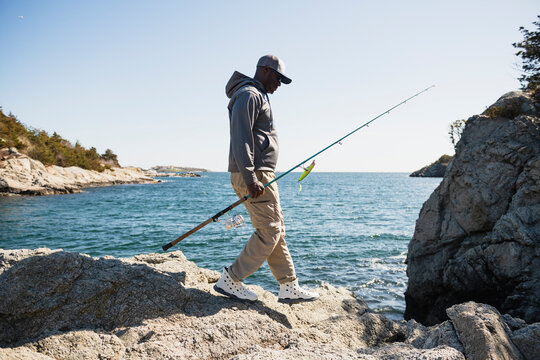 Black fisherman walks along a rocky coastline