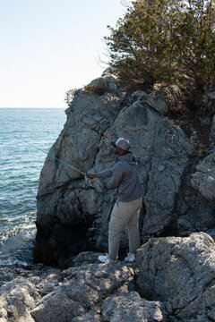 Black man fishing from rocks by the sea