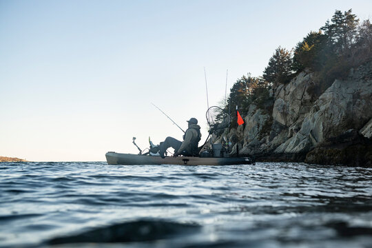 Man in fishing kayak floats by rocky coastline
