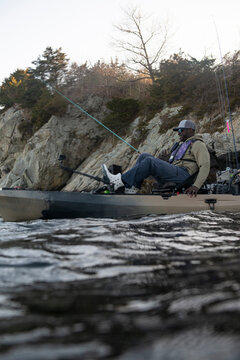 Man pedaling a fishing kayak near a rocky shoreline