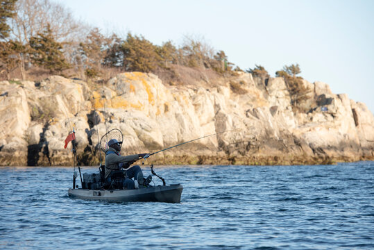 Man kayak fishing on the ocean near a rocky cliff